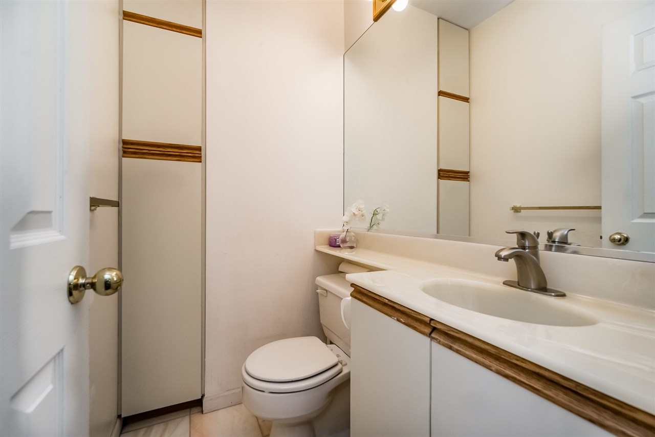 A bathroom, a vanity and mirror beside the toilet with a linen cupboard alongside.