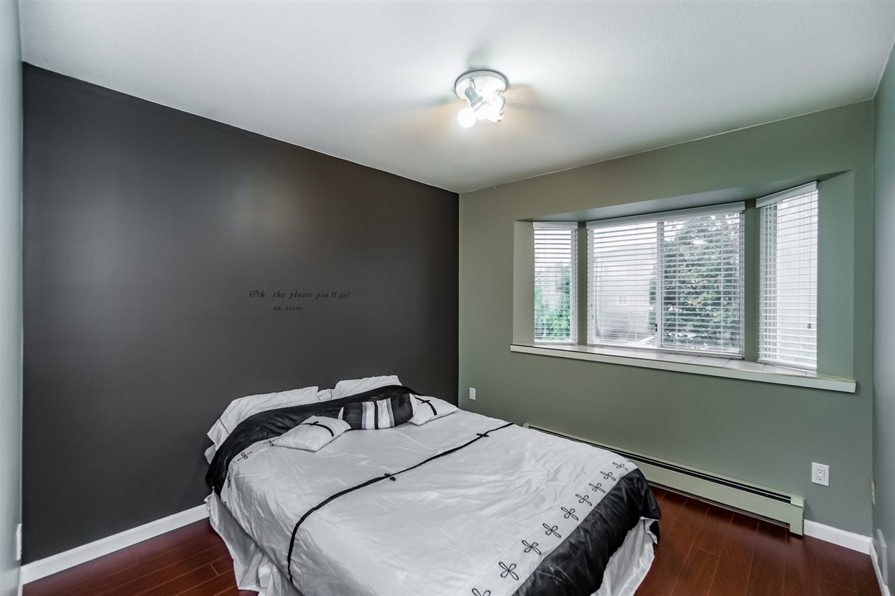 A bedroom with a dark feature wall, the bed under the window with the light coming through the blind.