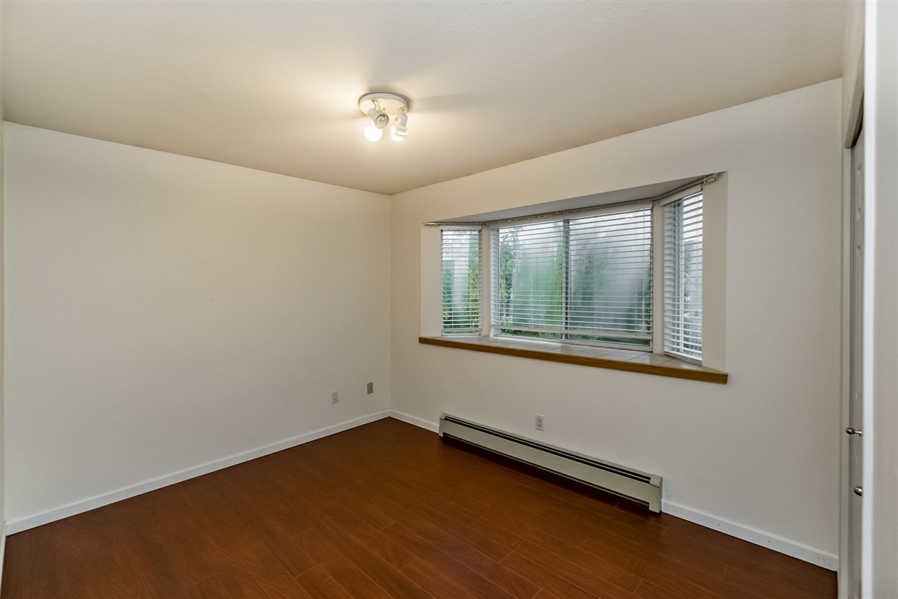 An empty bedroom, hardwood underfoot and a wide window along one wall.