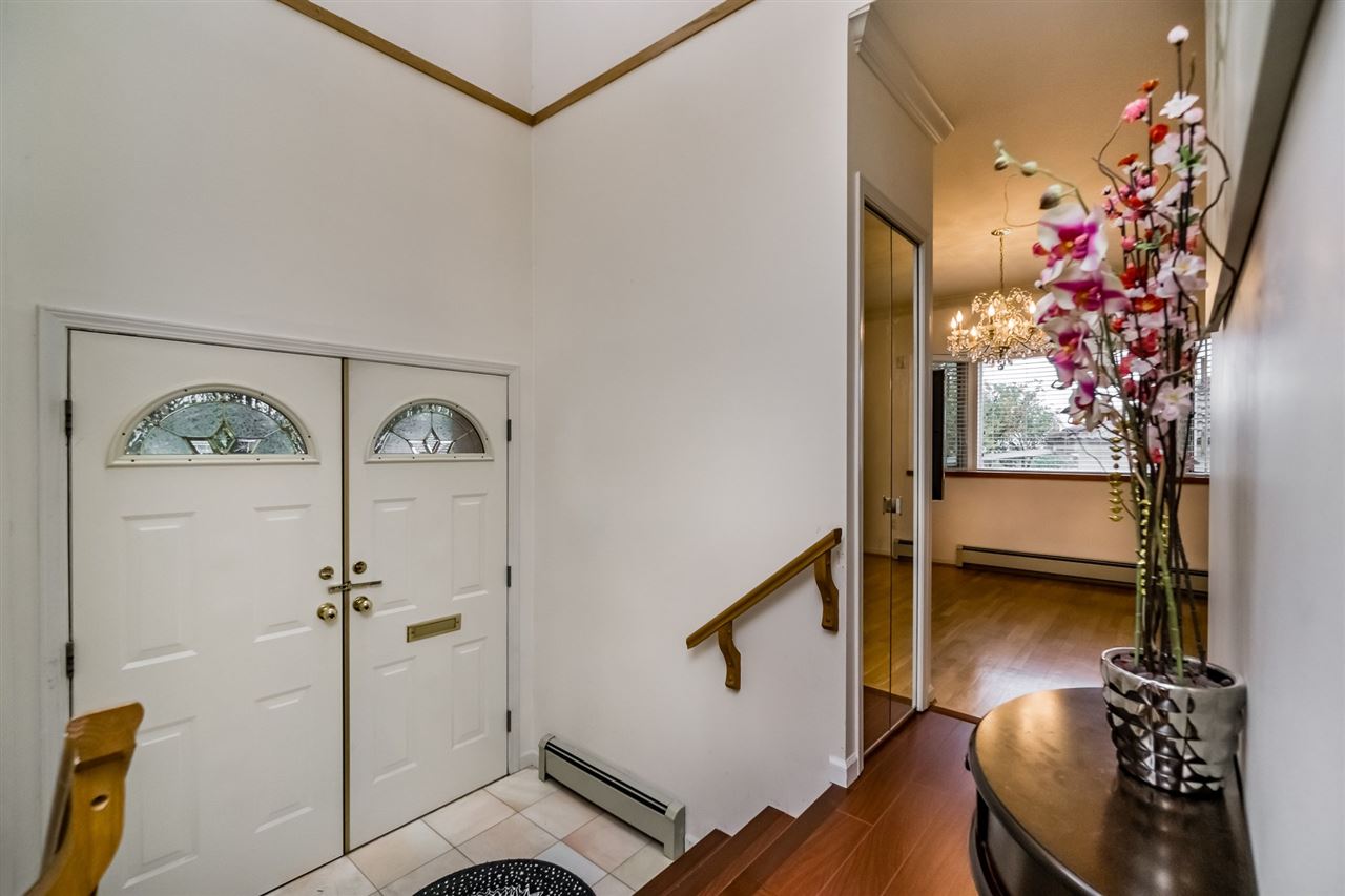 The foyer, the doors behind and the stair rising to the right past a flower arrangement.