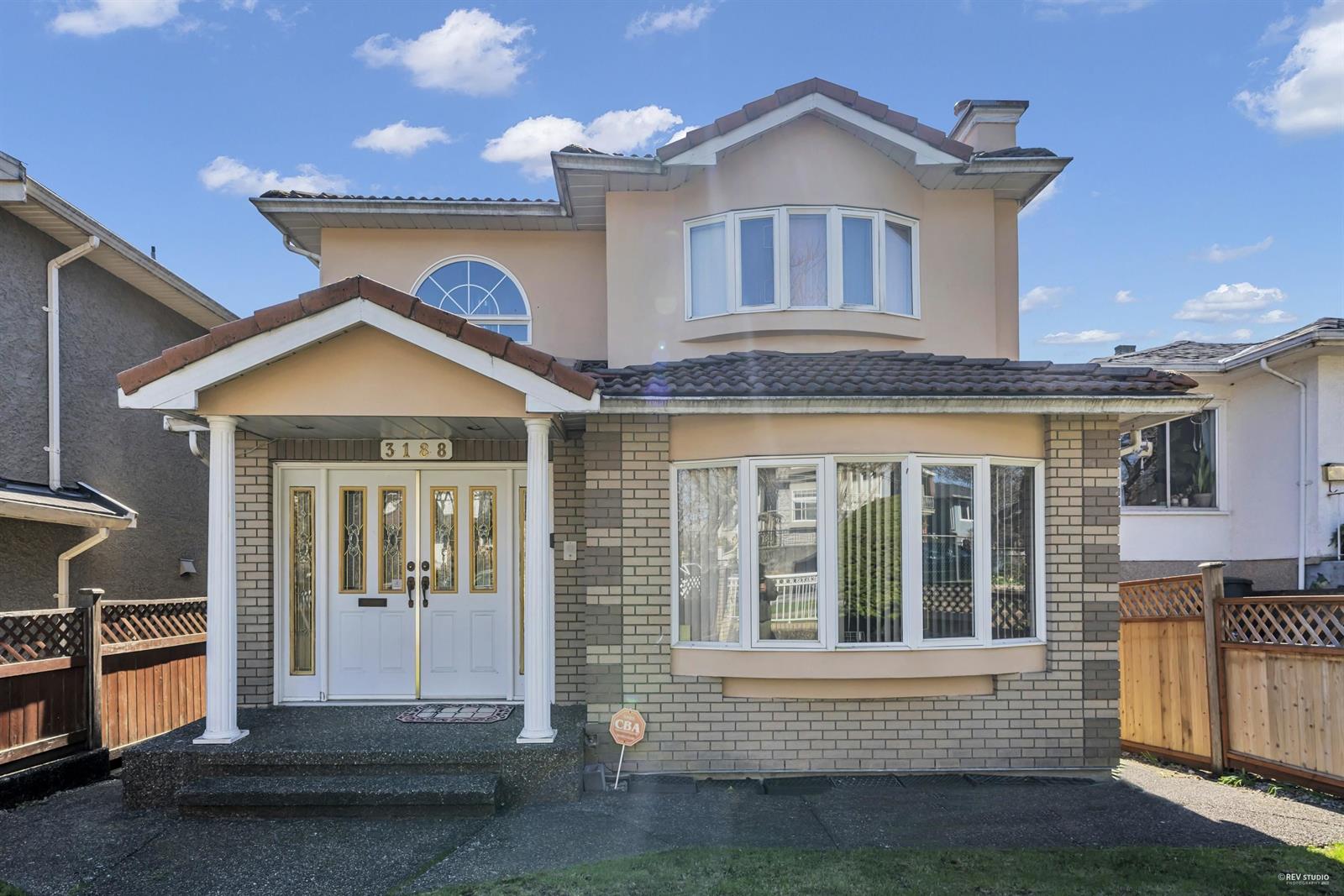 The front of the house, brick and pale stucco under a tiled roof, with a columned porch and a bay window beside it.