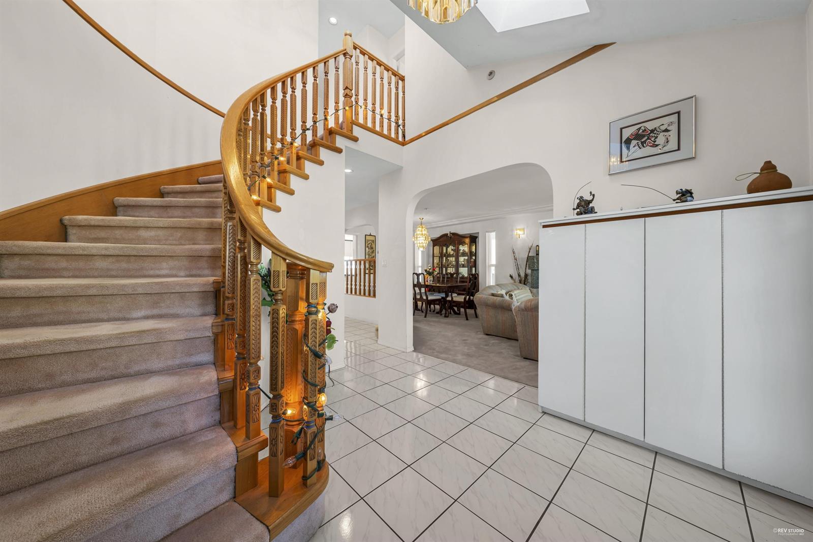 The entry hall, a curved timber staircase turning up under a skylight over pale tiled floor.