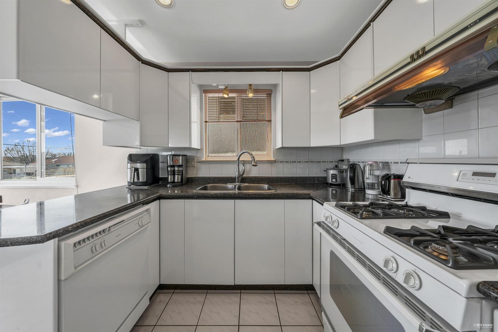 The kitchen, white cupboards set around a gas range under dark stone counters.
