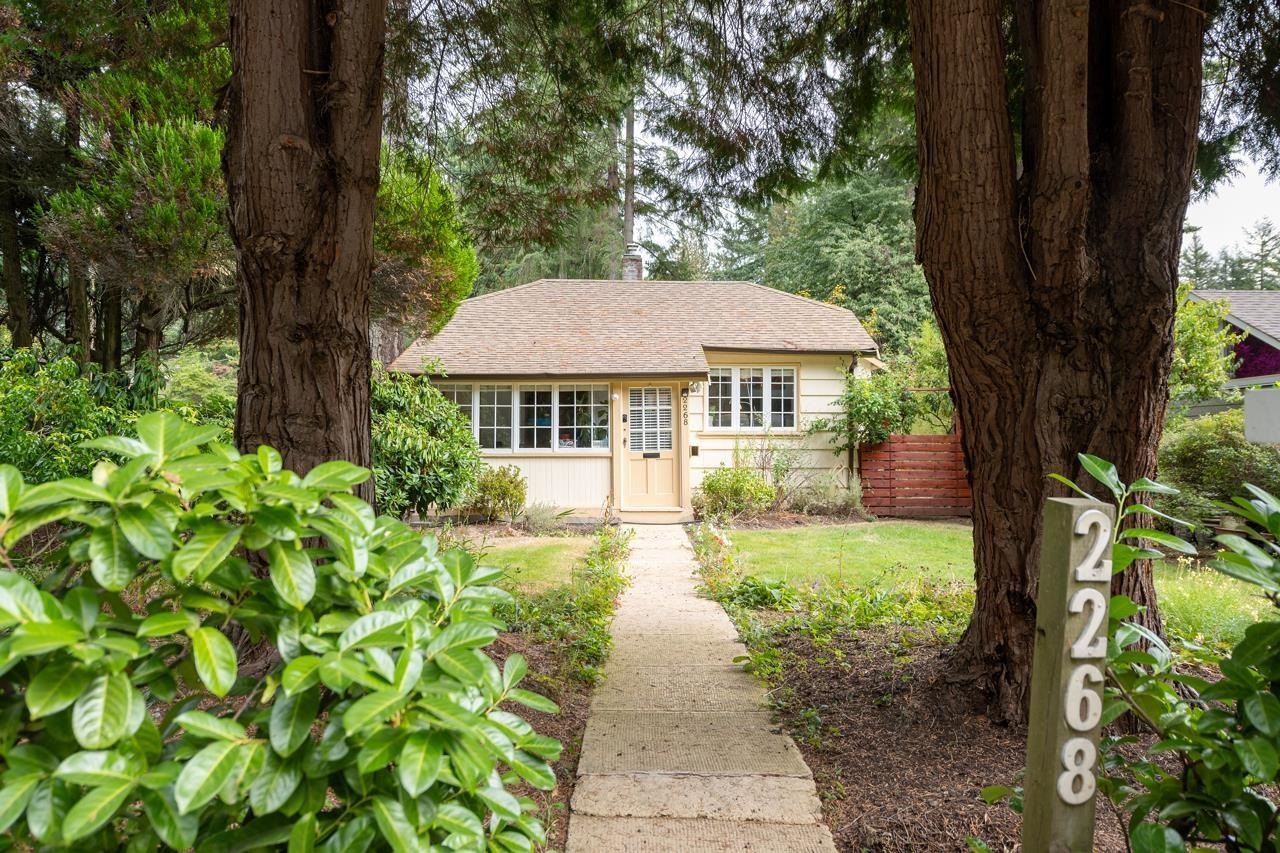 The bungalow at the end of its front path, seen between two tall cedars with the house number on the trunk of one.