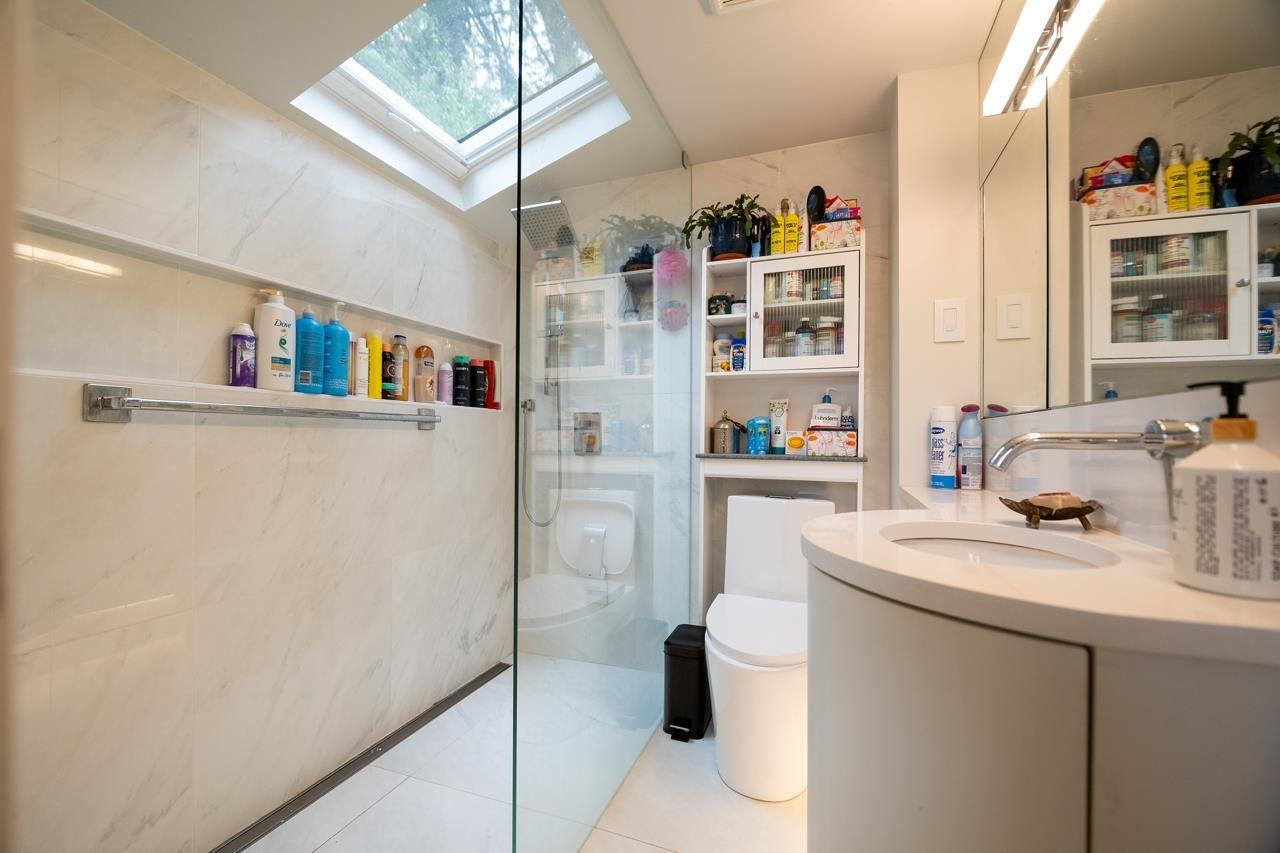 The bathroom, the glass shower on the left and the vanity on the right under a skylight.