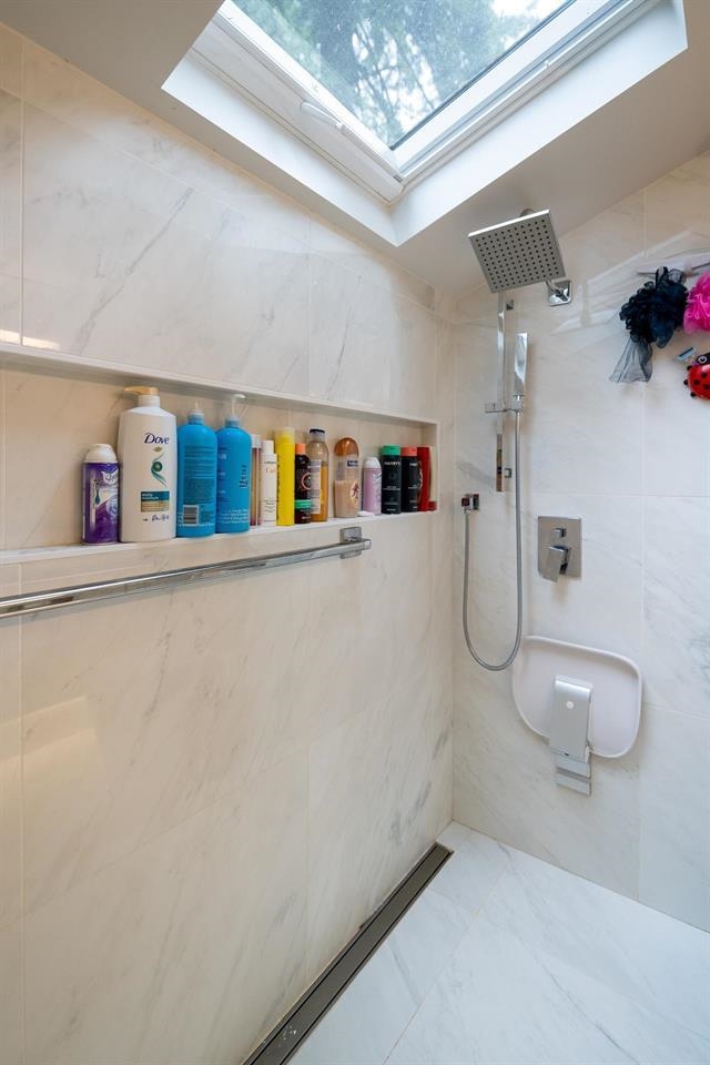The walk-in shower in marble, a recessed shelf along the wall and a skylight overhead.