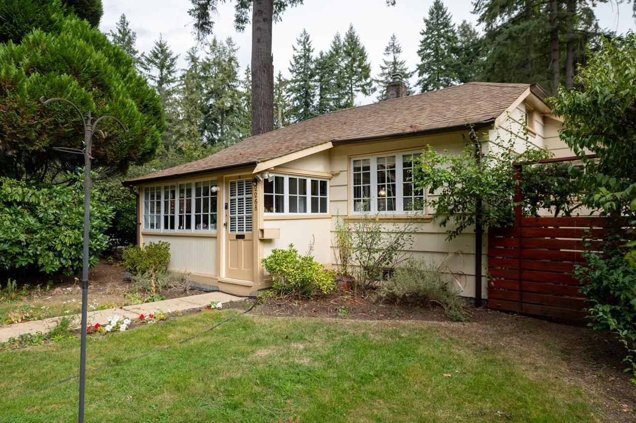 The house from the street, long and low behind a lawn, with a slatted fence running down one side.