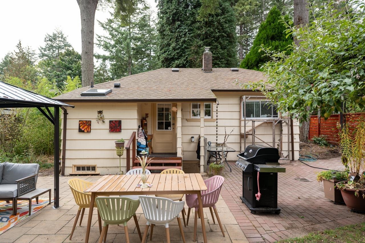 The rear of the bungalow from the patio, the barbecue at one side and chairs around the table.