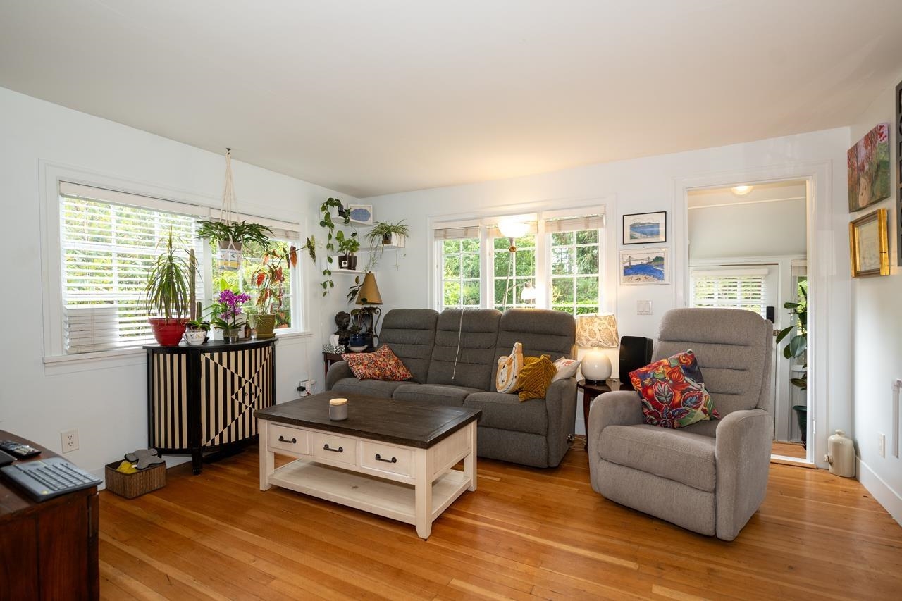The living room with windows on two sides and plants along the sills.