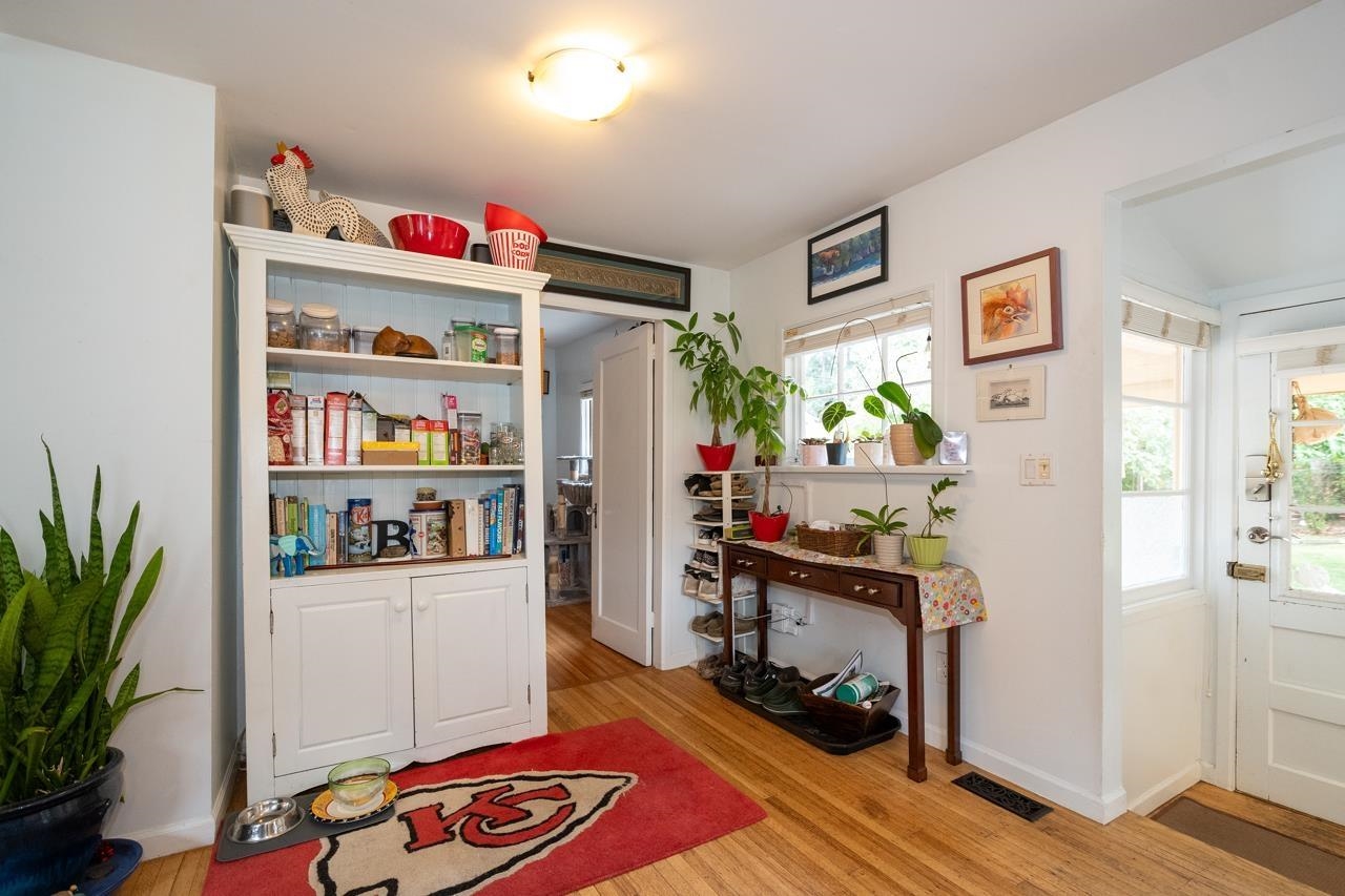 The end of the house by the side door, a tall white cabinet and a rug on the hardwood.