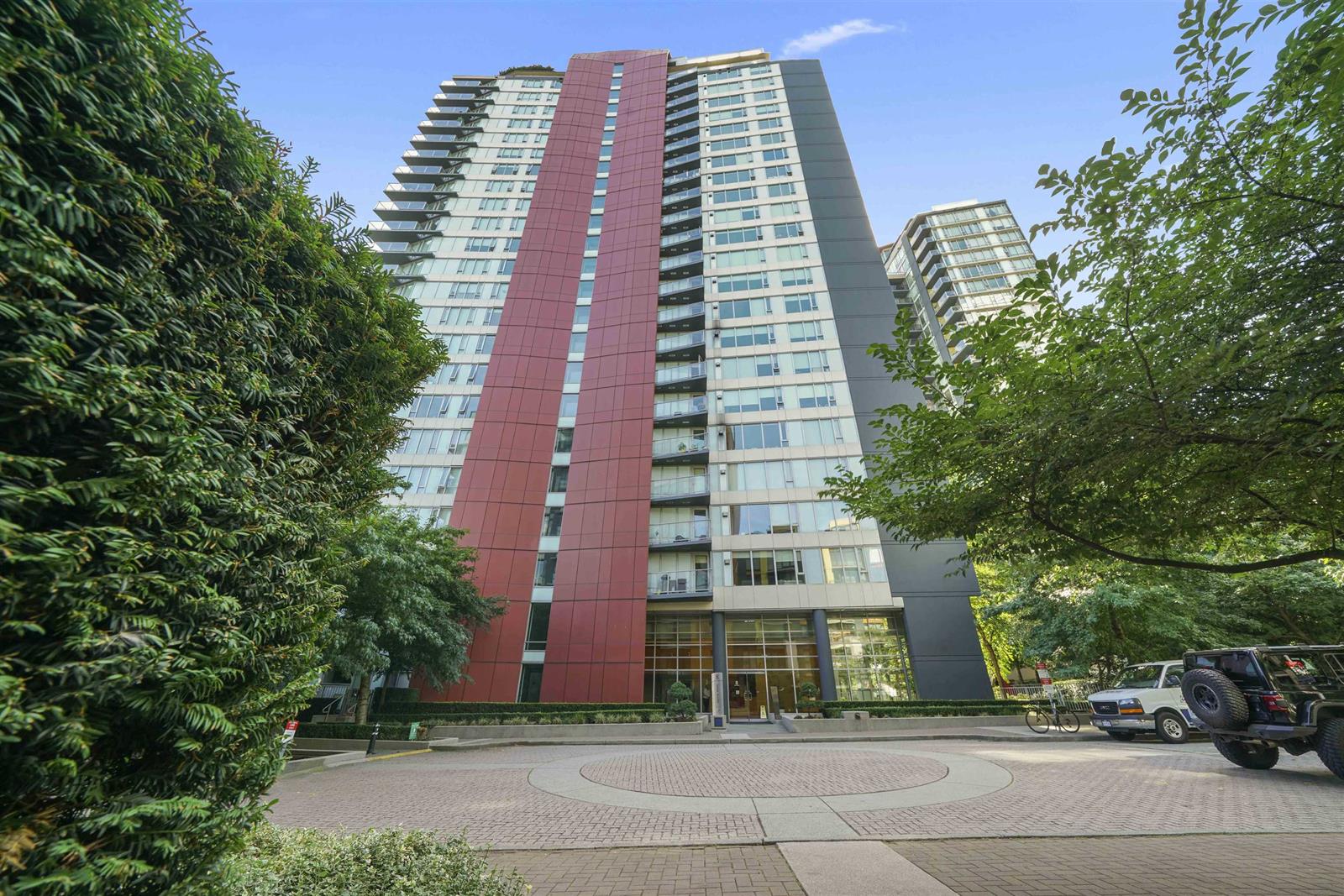 The tower from the street, red panels running up its face between the trees.