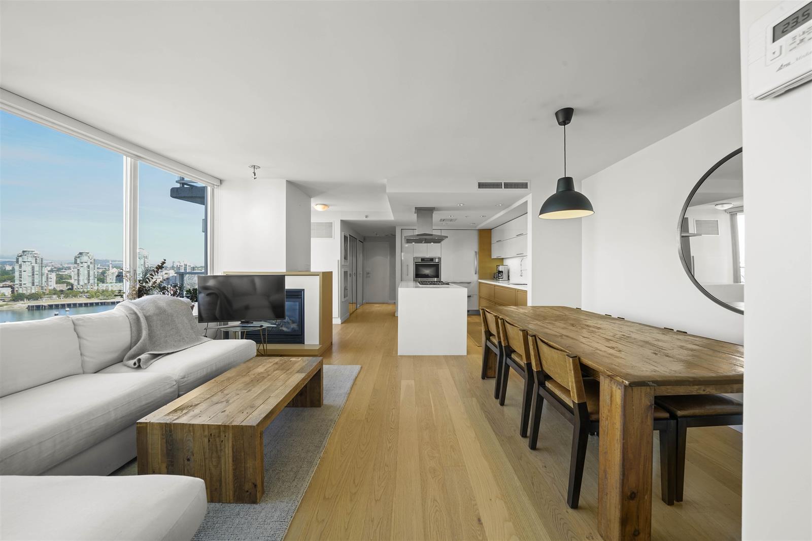 The living and dining rooms running together, a long timber table beside the kitchen island.