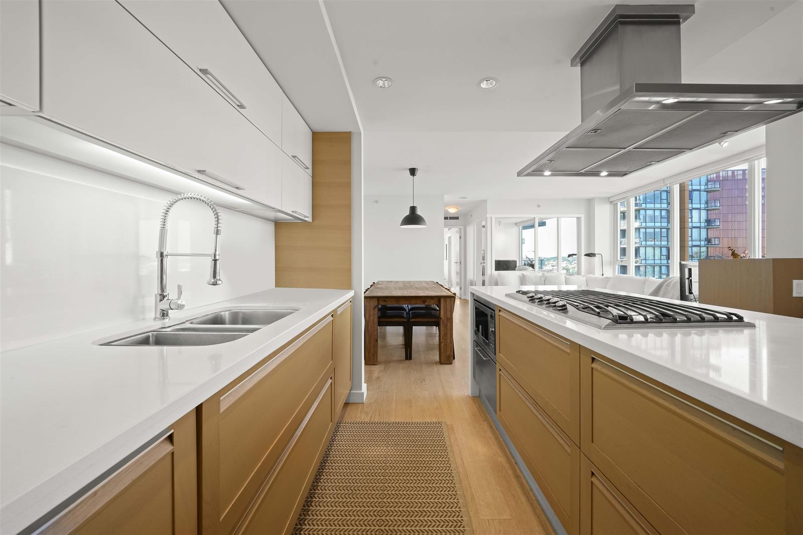 The kitchen along its length, a gas cooktop under a stainless hood with the city in the windows beyond.