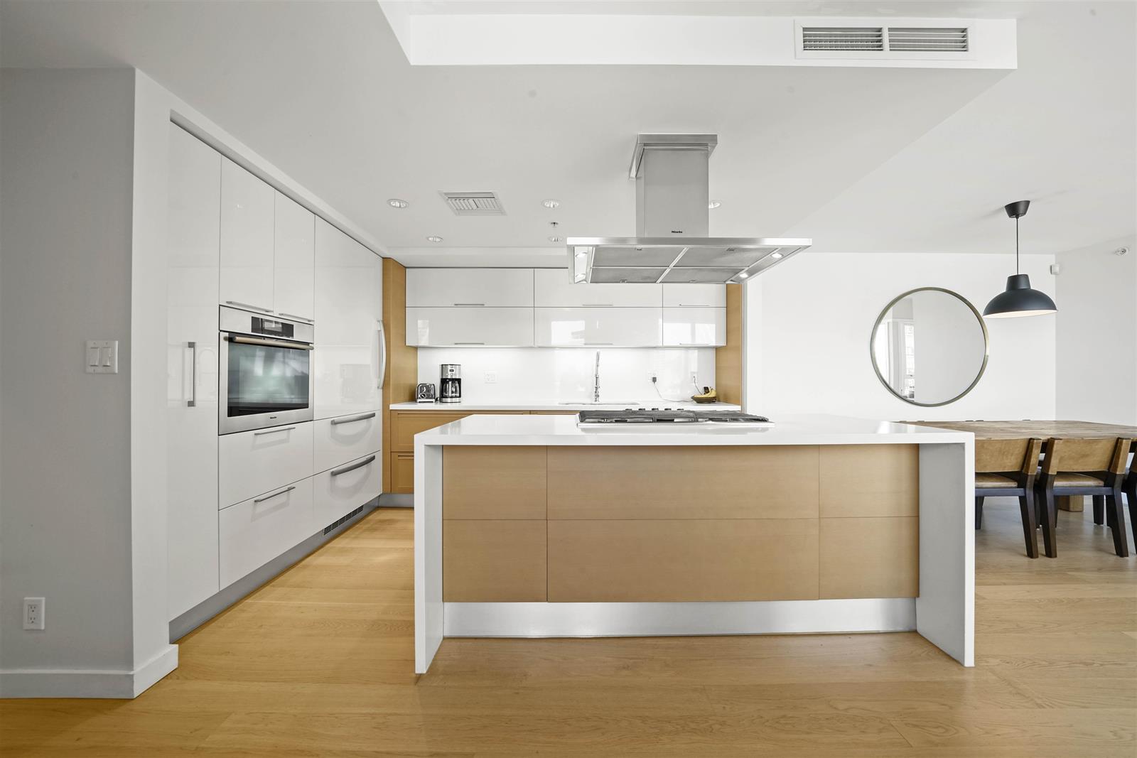 The kitchen island in pale timber, with wall ovens set into the run behind it.