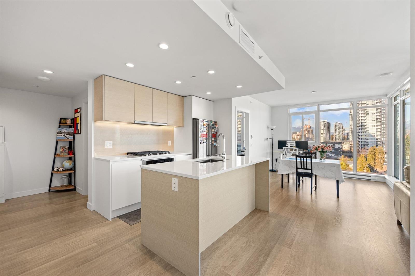 The kitchen from the hall, the island in front and the dining area at the windows.