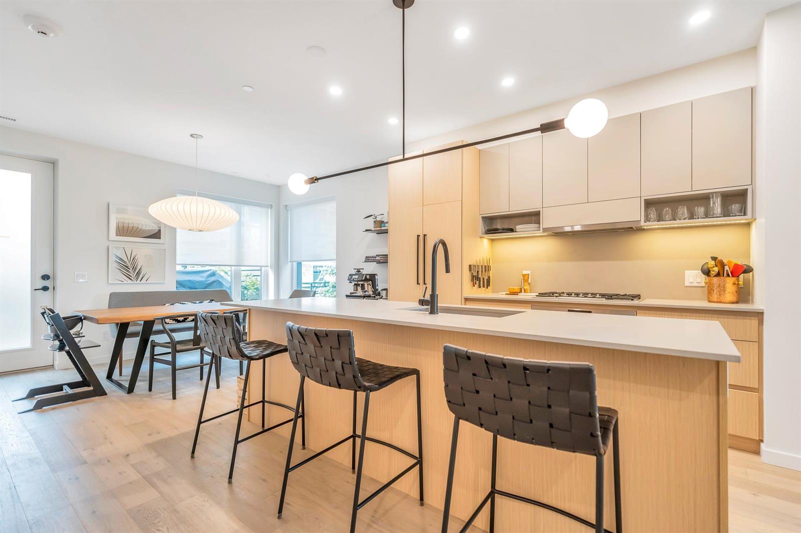 The kitchen island with stools along it, the dining table beyond and the room running on to the windows.