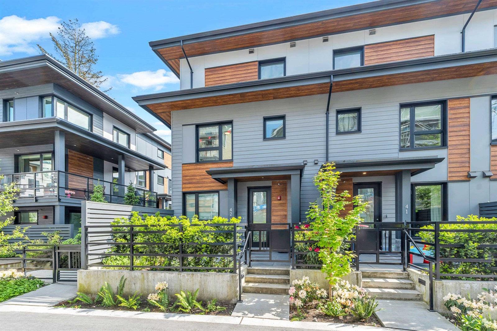 The terrace from the street, timber and dark cladding above a planted frontage.