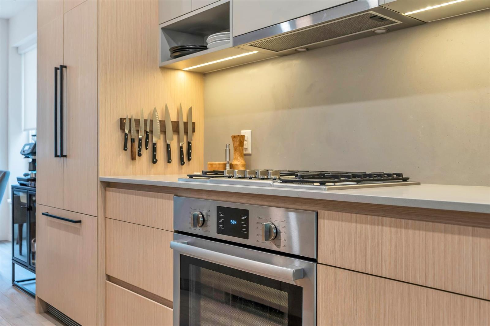 The cooking wall, a gas cooktop and wall oven set into pale cabinets under a metallic splashback.