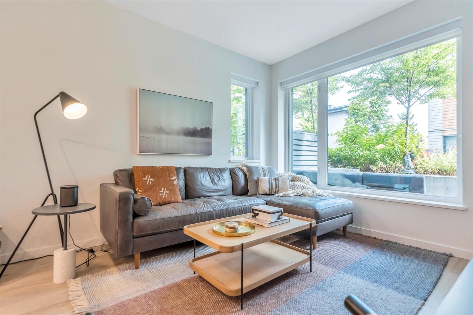The living room, a sofa beneath a tall window with the trees outside.