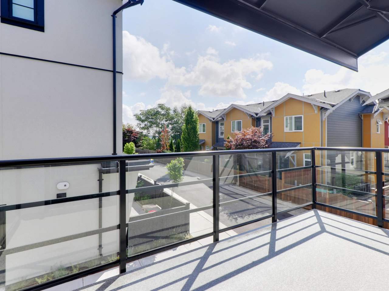 The balcony, a glass rail with the roofs of the neighbouring homes beyond.