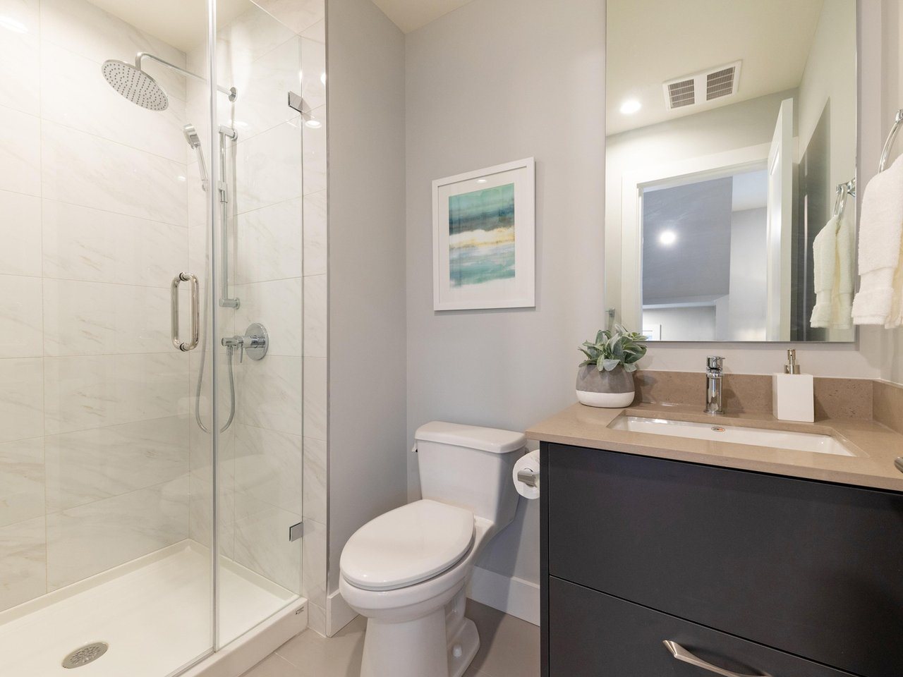 A bathroom, a glass shower beside the vanity and a framed print above the toilet.