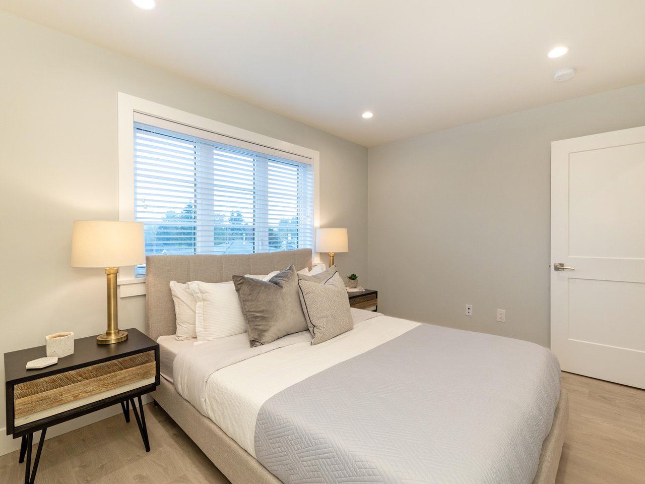 The primary bedroom, a bed between two windows with the ensuite door beyond.