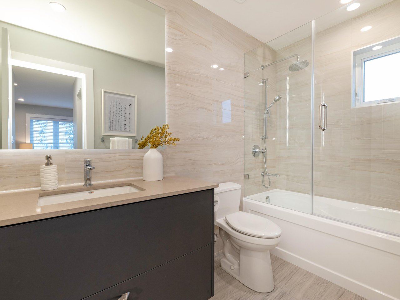 The ensuite, a glass shower next to the tub with tiled walls throughout.