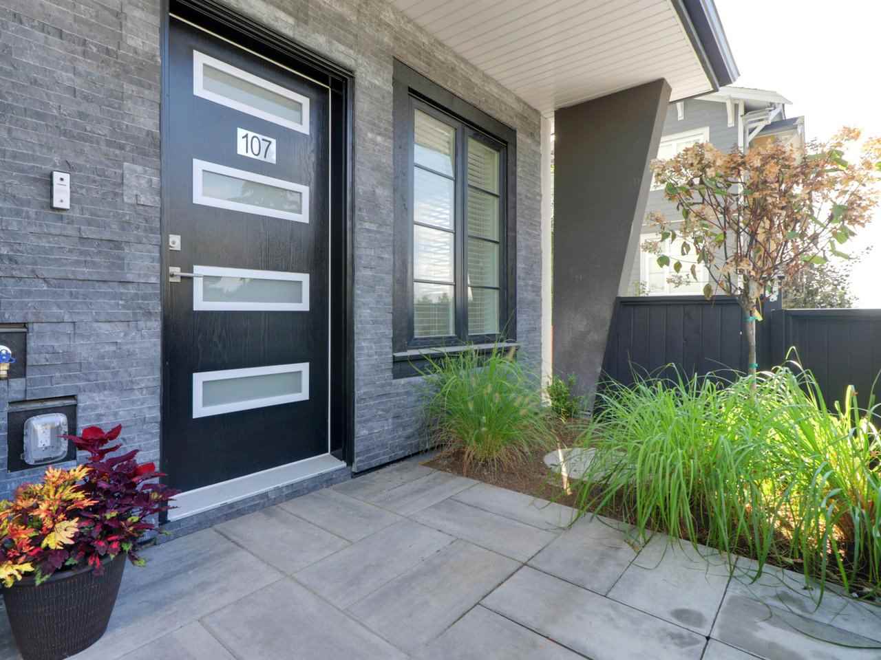 The entry, a black door with narrow glass panels beside it and planting along the paved path.