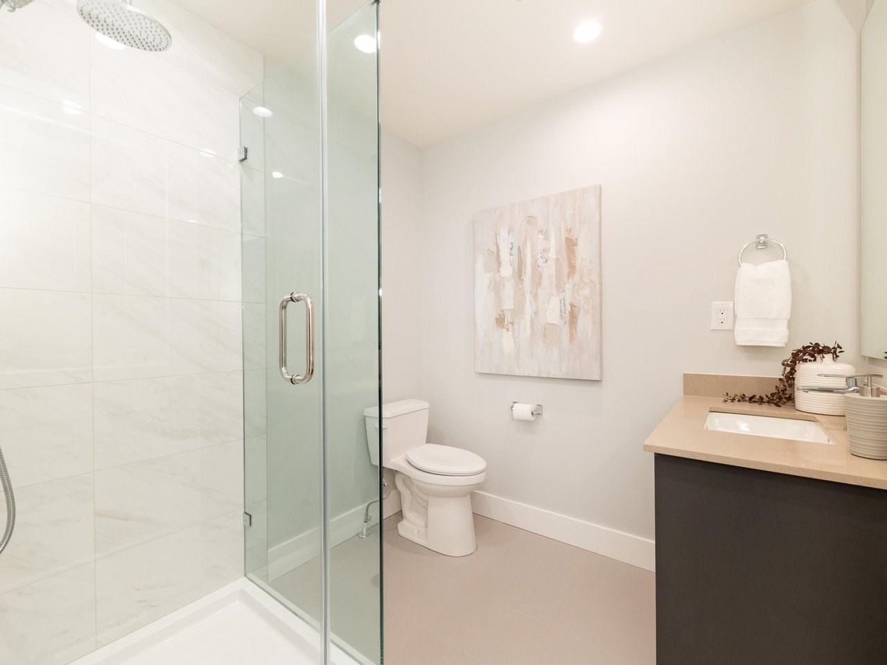 A second bathroom, a glass shower beside a vanity under a framed print.