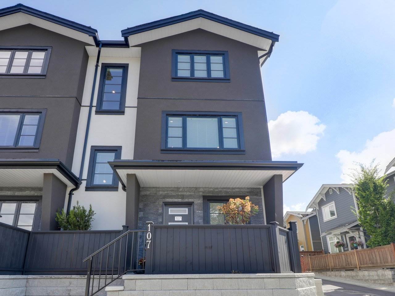 The building from the street, three storeys of dark siding and white trim with a railed stair up to the door.