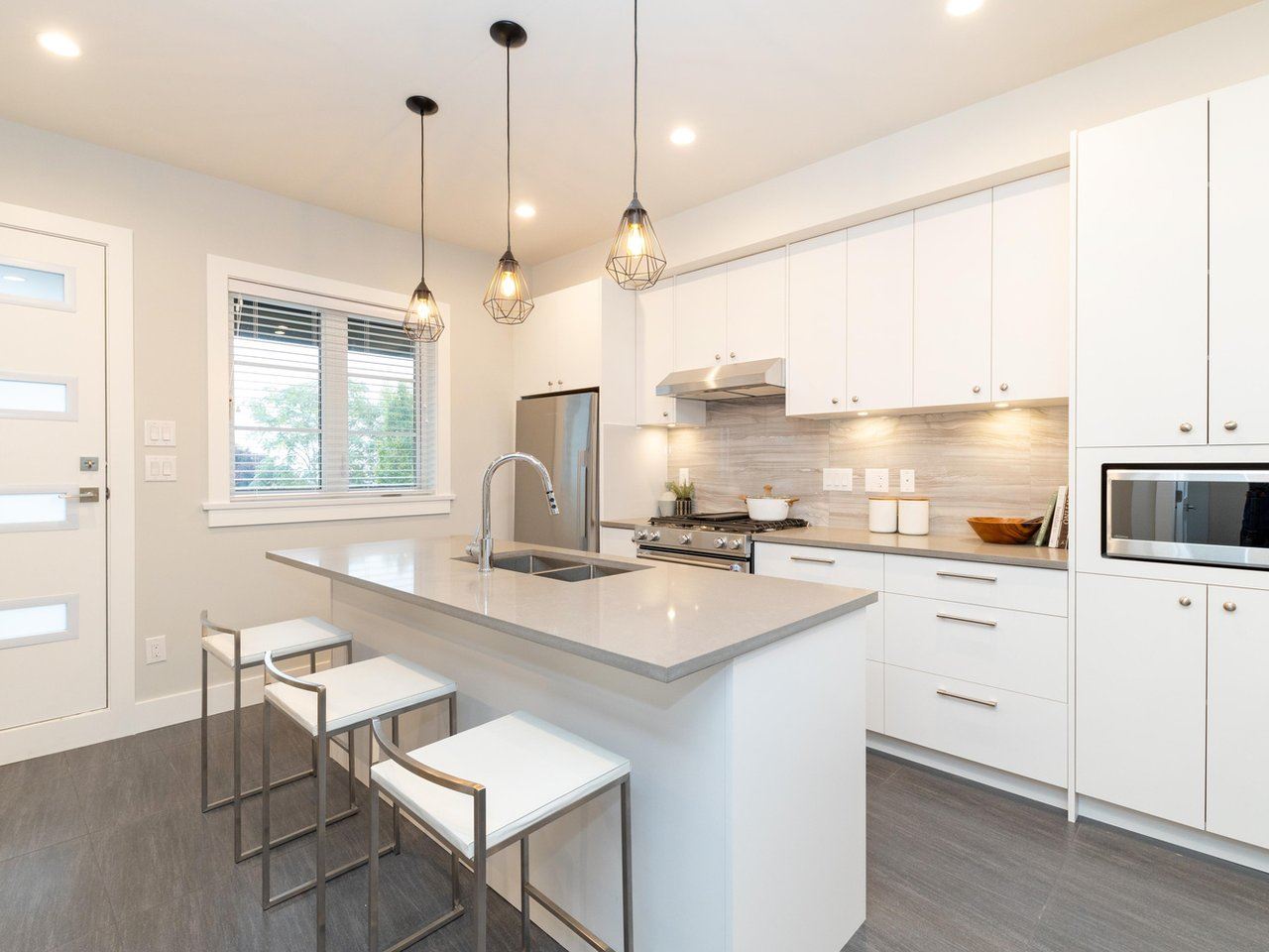 The kitchen, a white island with stools and pendant lights hanging over it.