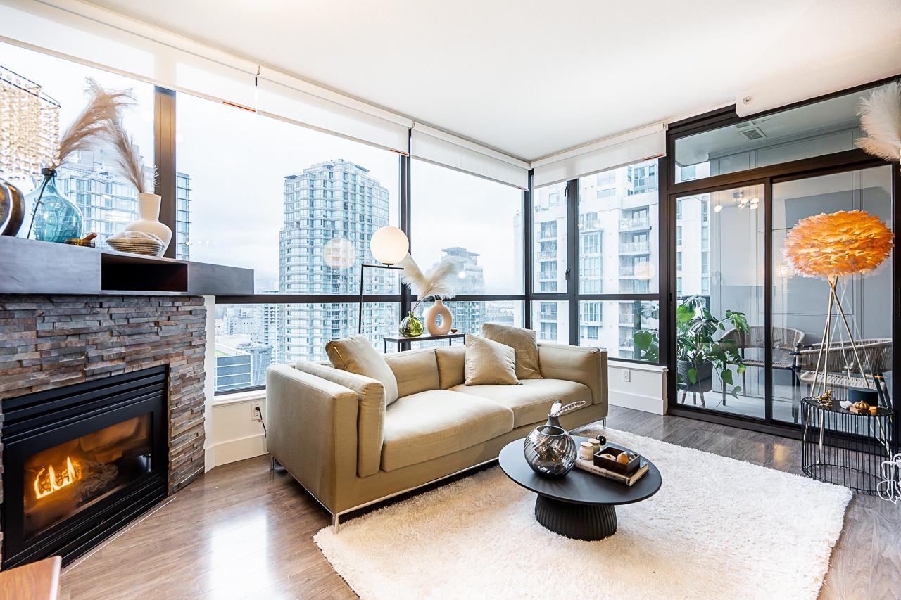 The living room from the fireplace side, a sofa on a pale rug and the corner glass looking out to the city.