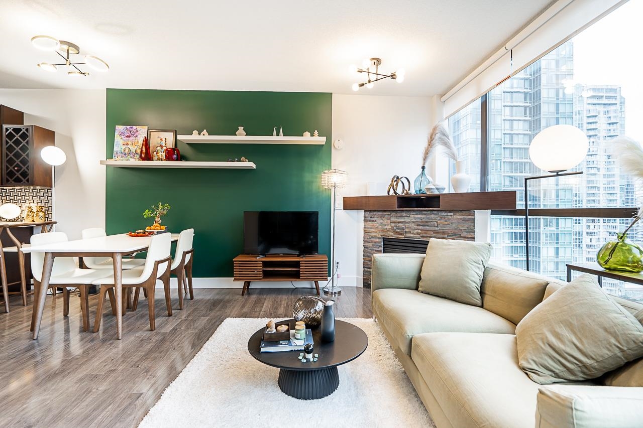 The living room and dining table together, the green feature wall behind and the television against the glass.