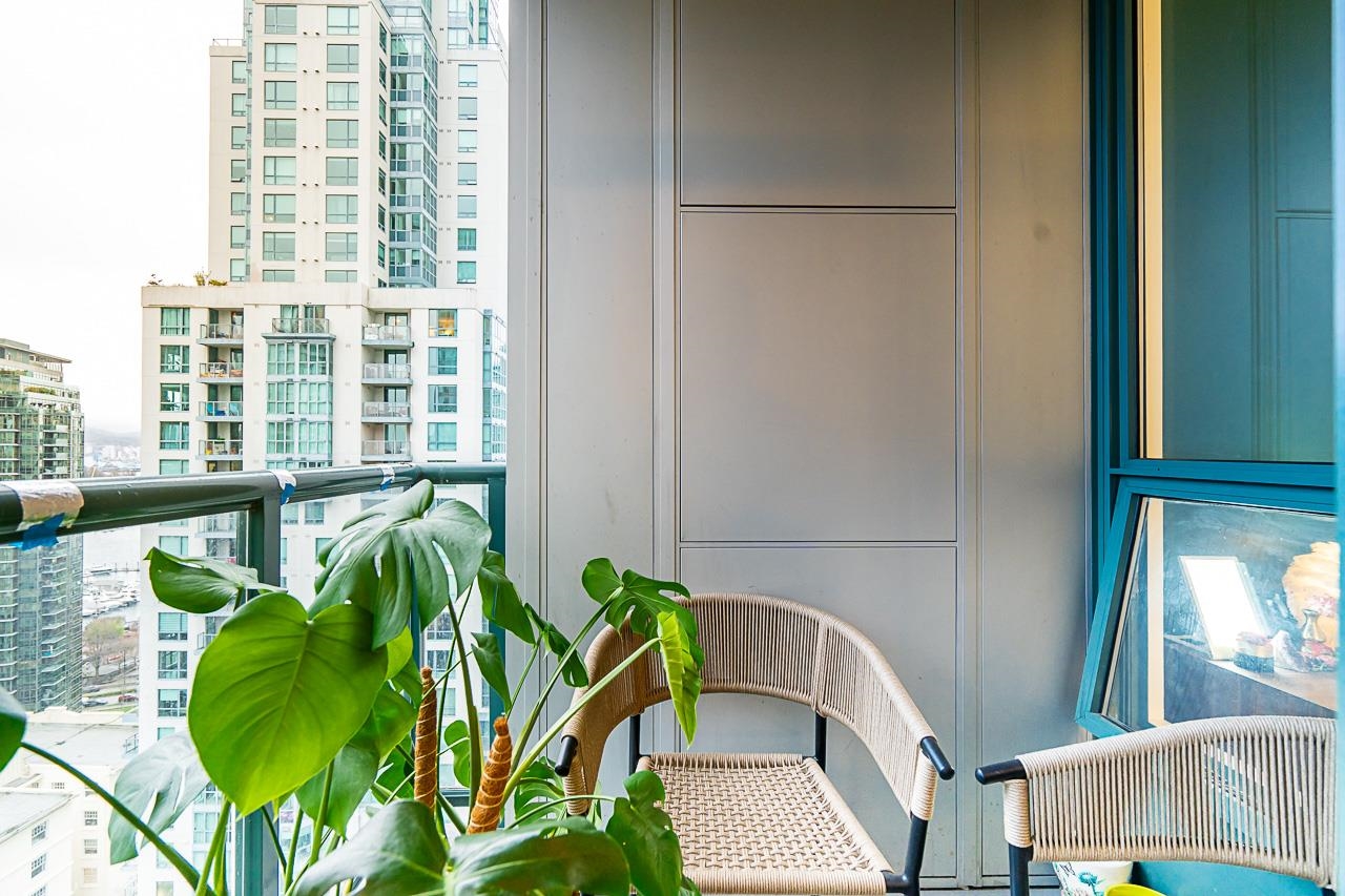 The balcony with a chair and a large potted plant, the neighbouring tower beyond the rail.
