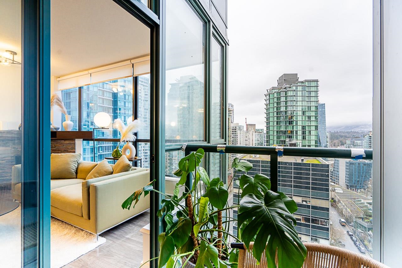 The view from the balcony back into the living room, plants in the foreground and the city to the right.