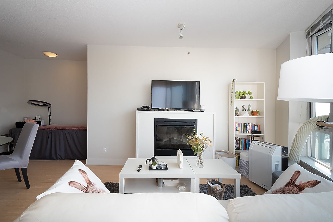 The living room across the fireplace, the television above it and the bedroom visible beyond the partition.