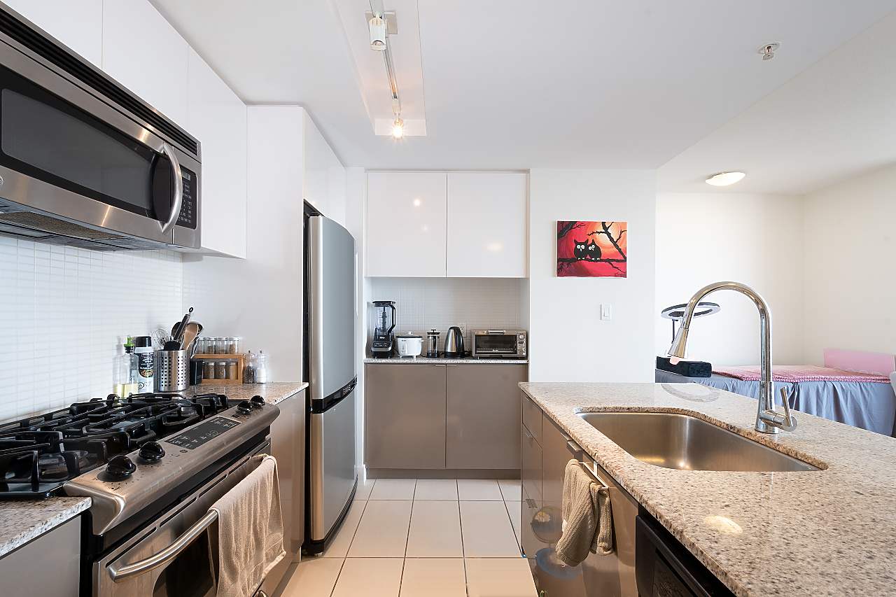 The kitchen along its length, the gas range and the microwave over it, the sink on the island opposite.