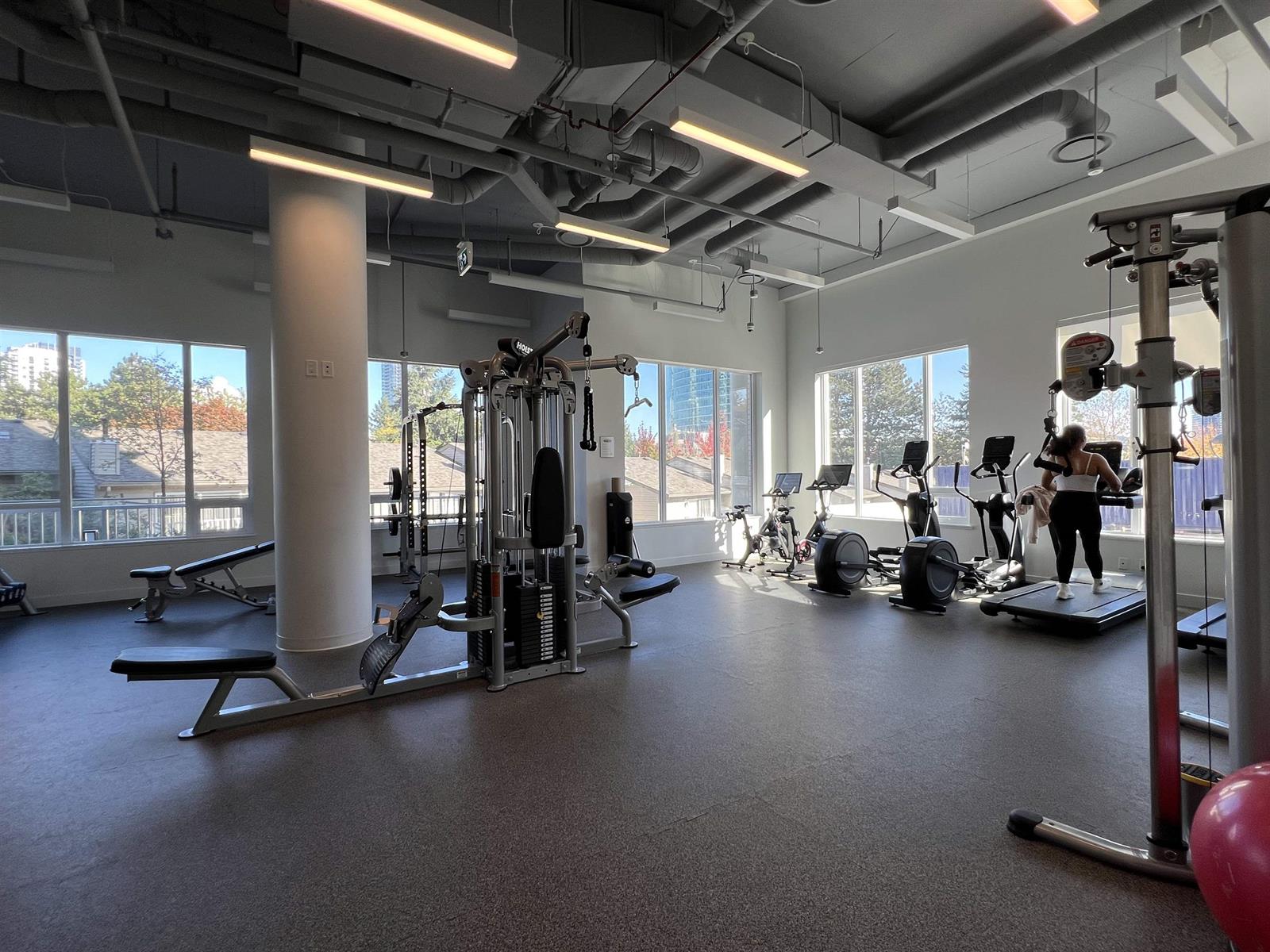 The gym, machines along a glazed wall under an exposed ceiling.