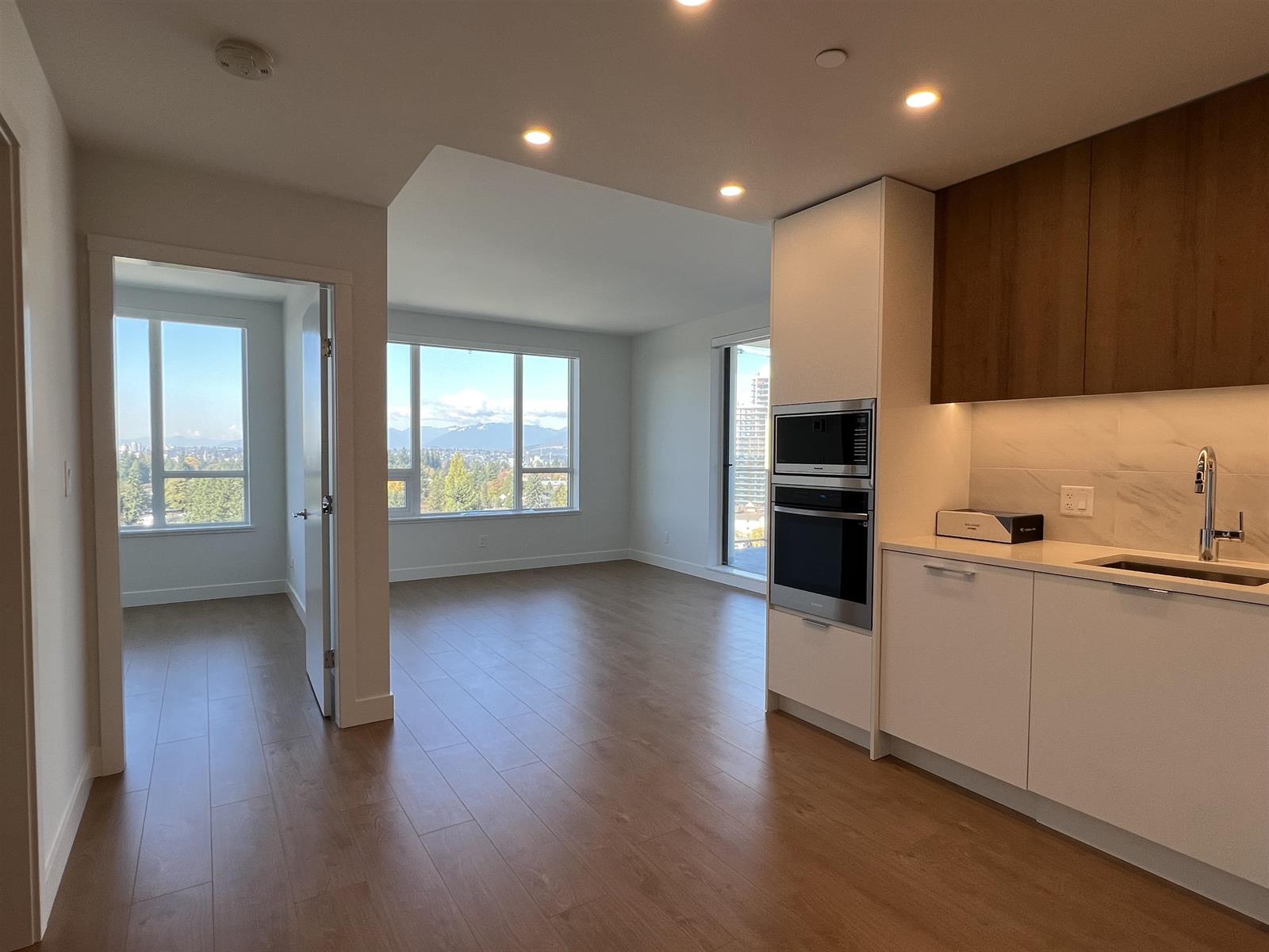 The living room, the kitchen run along the right and corner windows at the far end.