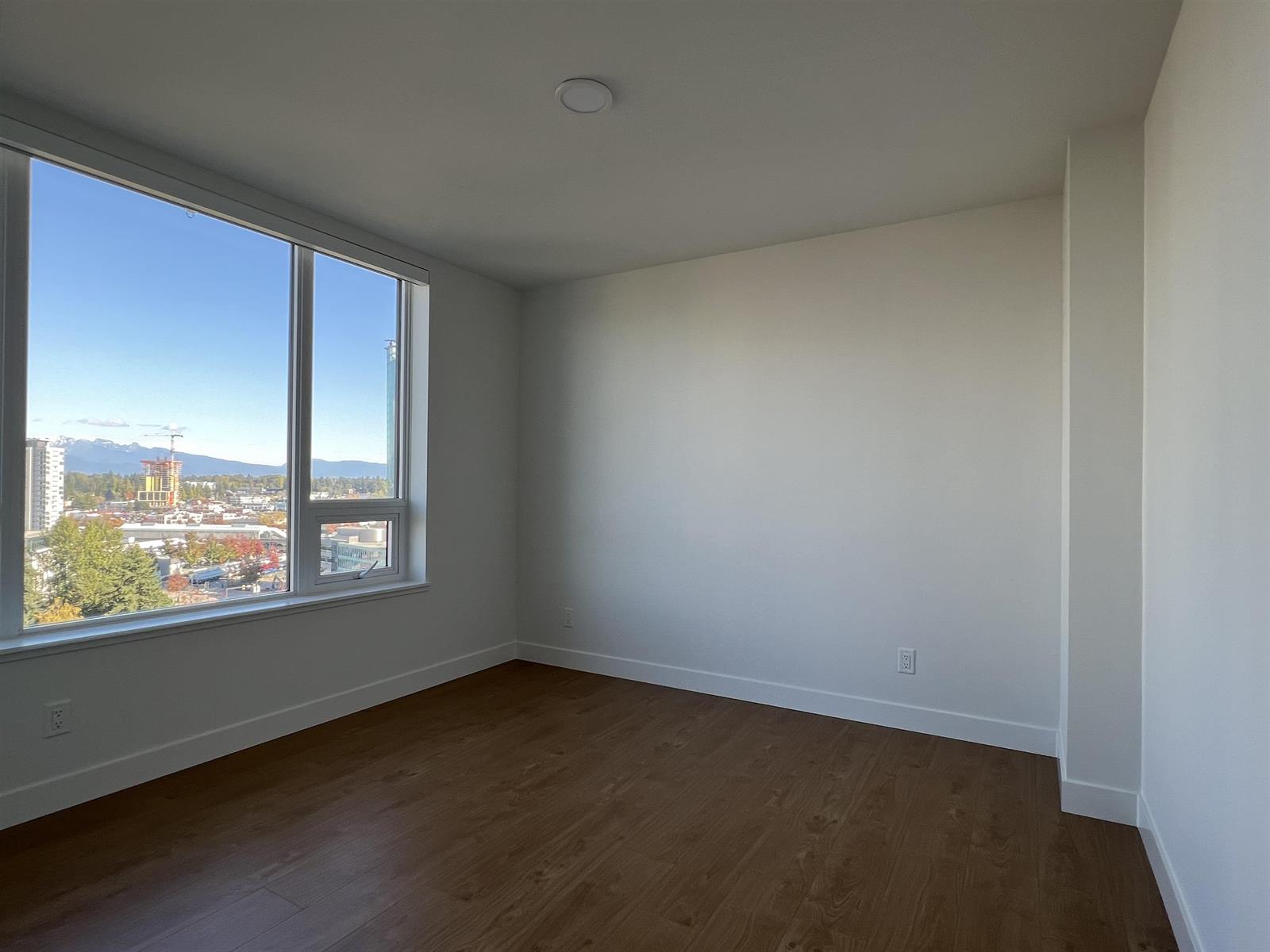 A bedroom with windows turning the corner, empty, on laminate boards.