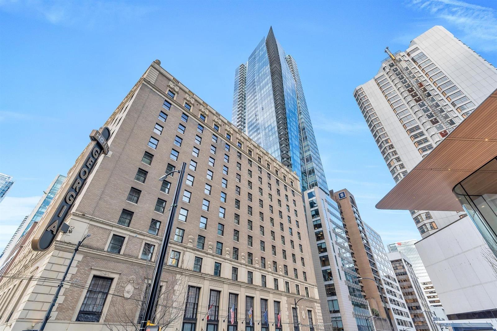 The building from the street corner, the stone of the Hotel Georgia in the foreground and the glass residence tower rising behind it.