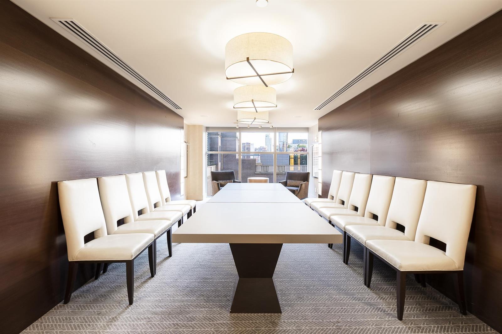 The boardroom, a long table with chairs on both sides beneath two drum lights.