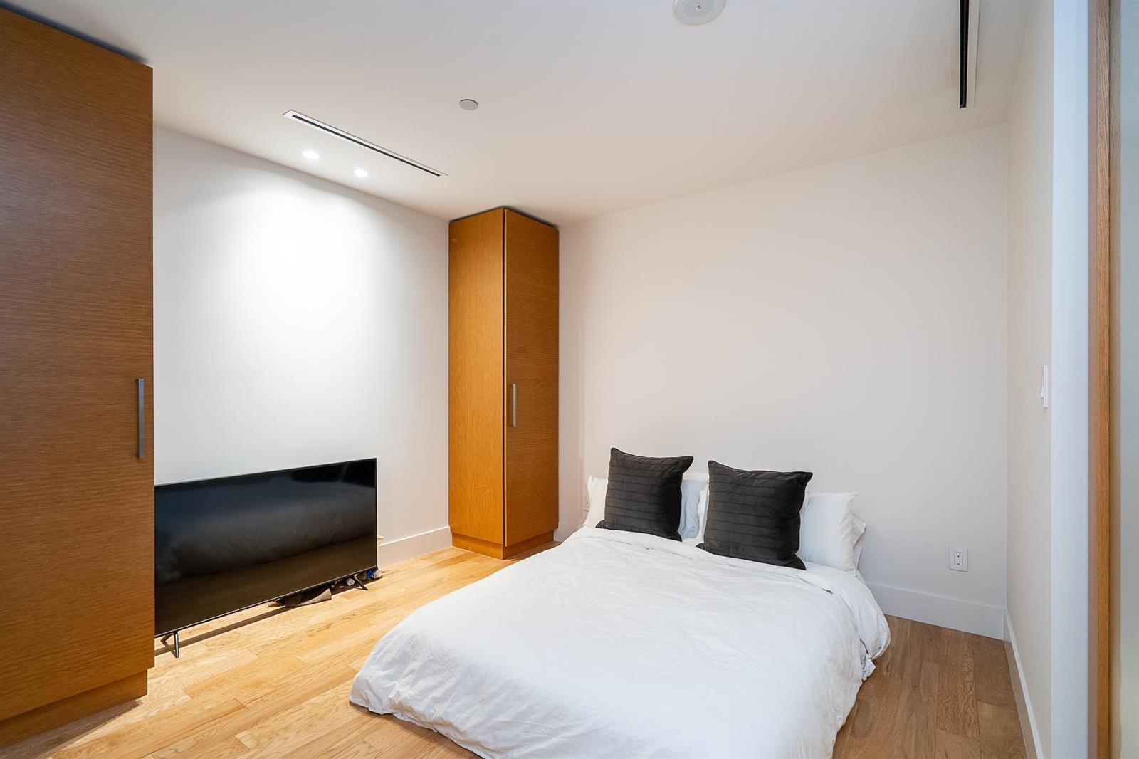 The second bedroom, a bed against the window wall with tall wood cabinetry along one side.
