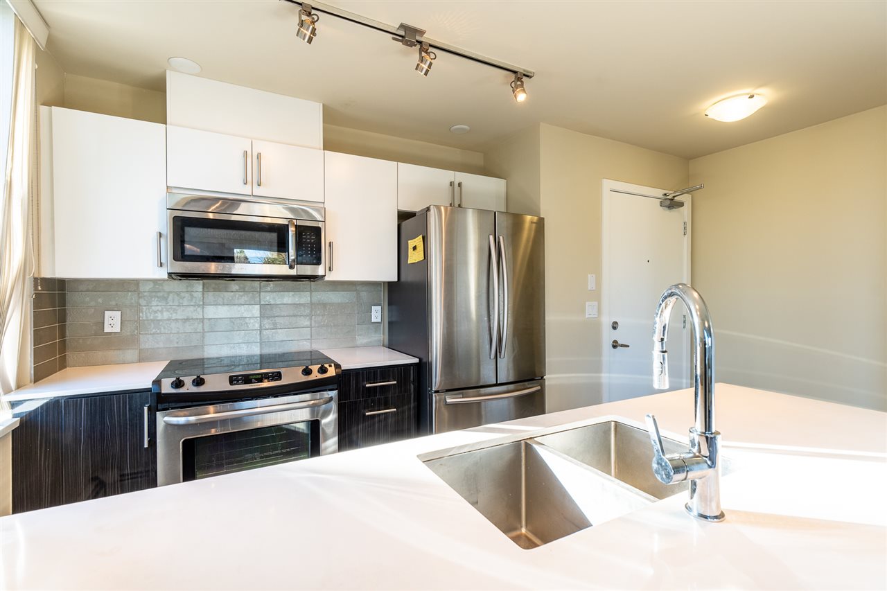 The kitchen from across the peninsula, stainless steel appliances and a tiled backsplash.