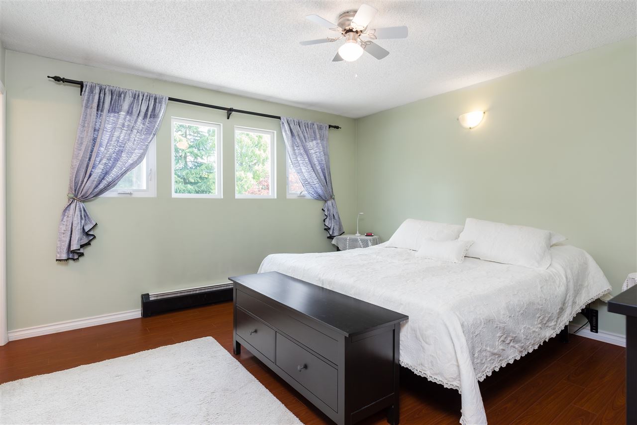 The primary bedroom, the bed against a green wall with a bench at its foot and a ceiling fan above.