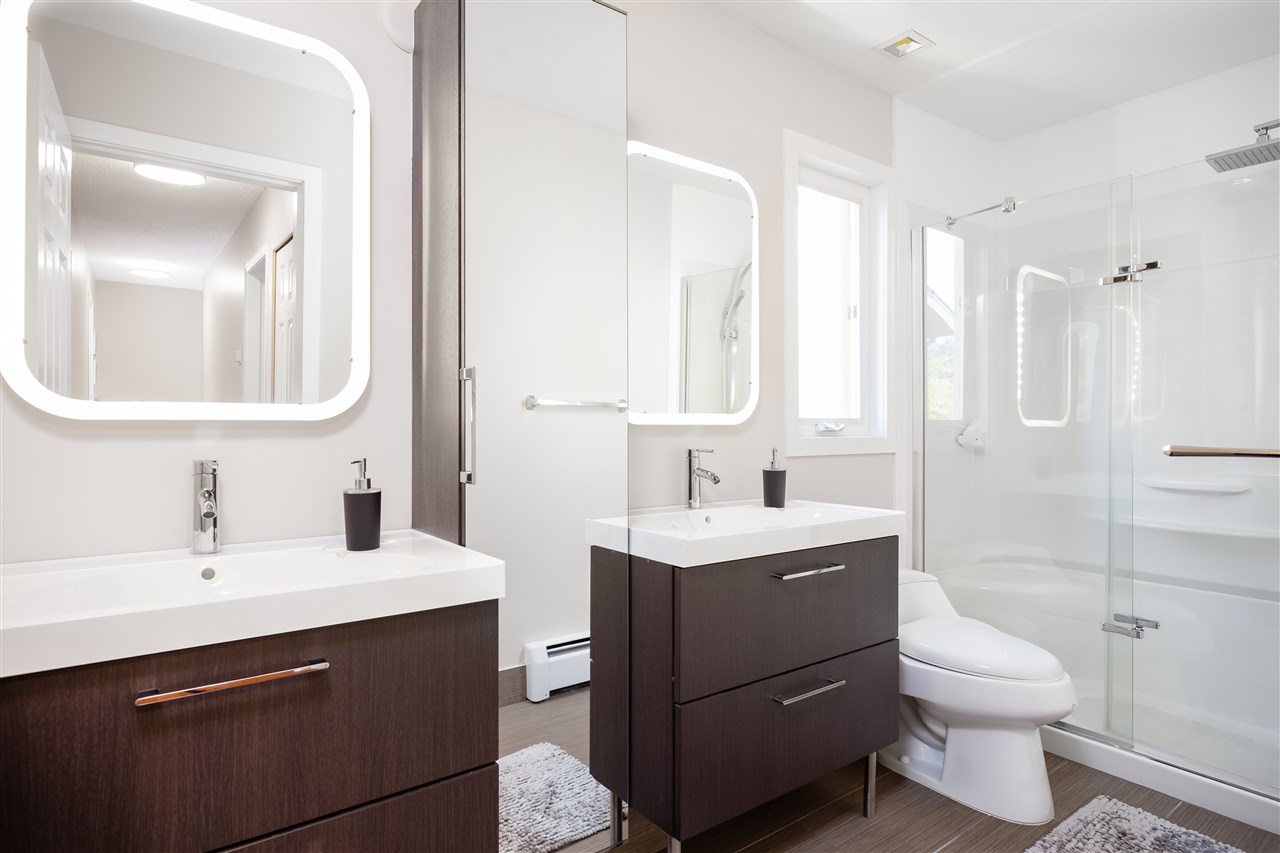 The ensuite, two dark vanities under lit mirrors with the glass shower alongside.