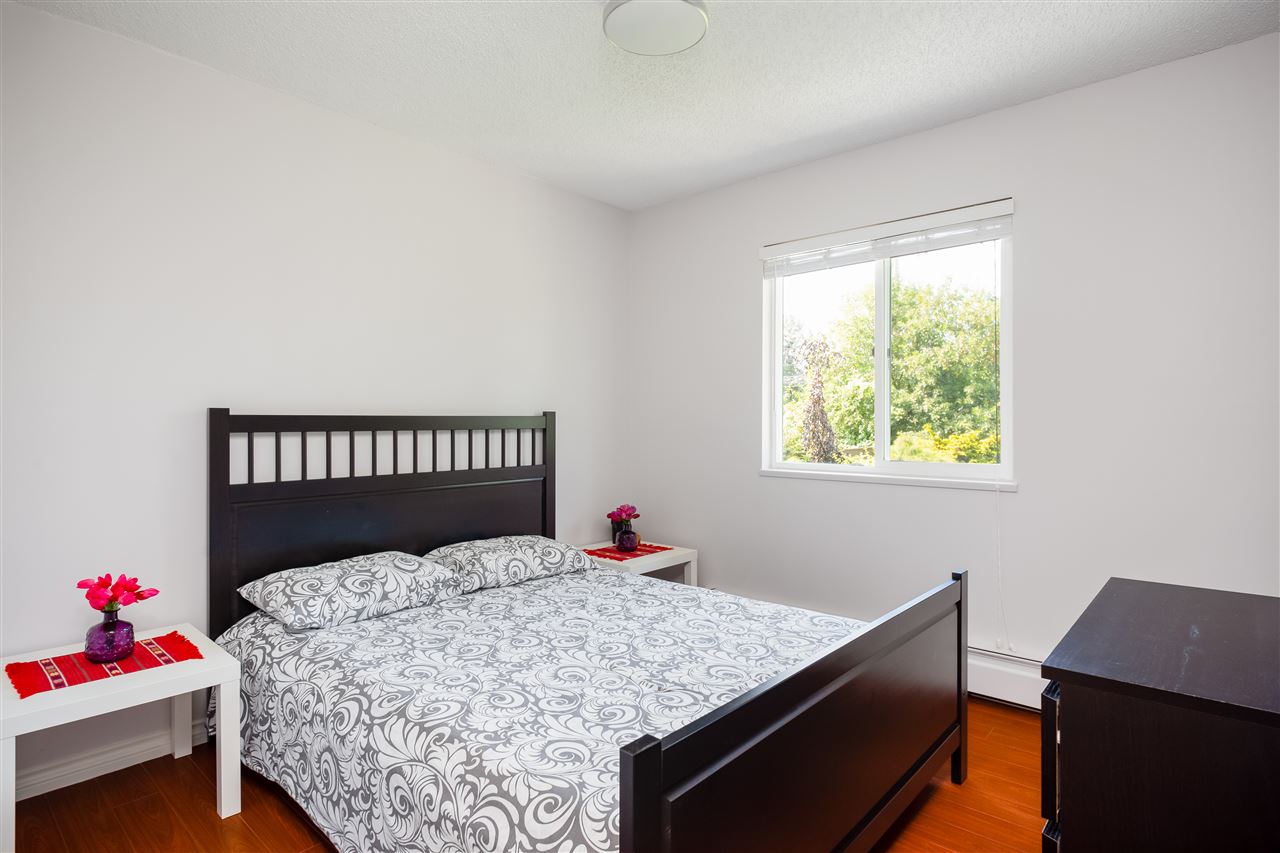 A bedroom, the dark wooden bed frame with the window looking into the greenery.