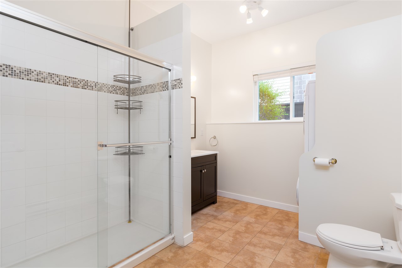 A bathroom, a wide glass shower beside a dark vanity with a tiled border along the wall.
