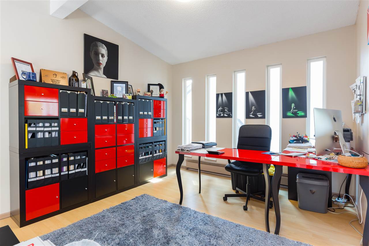 The lower study, red shelving along one wall with the desk and chair on the rug.