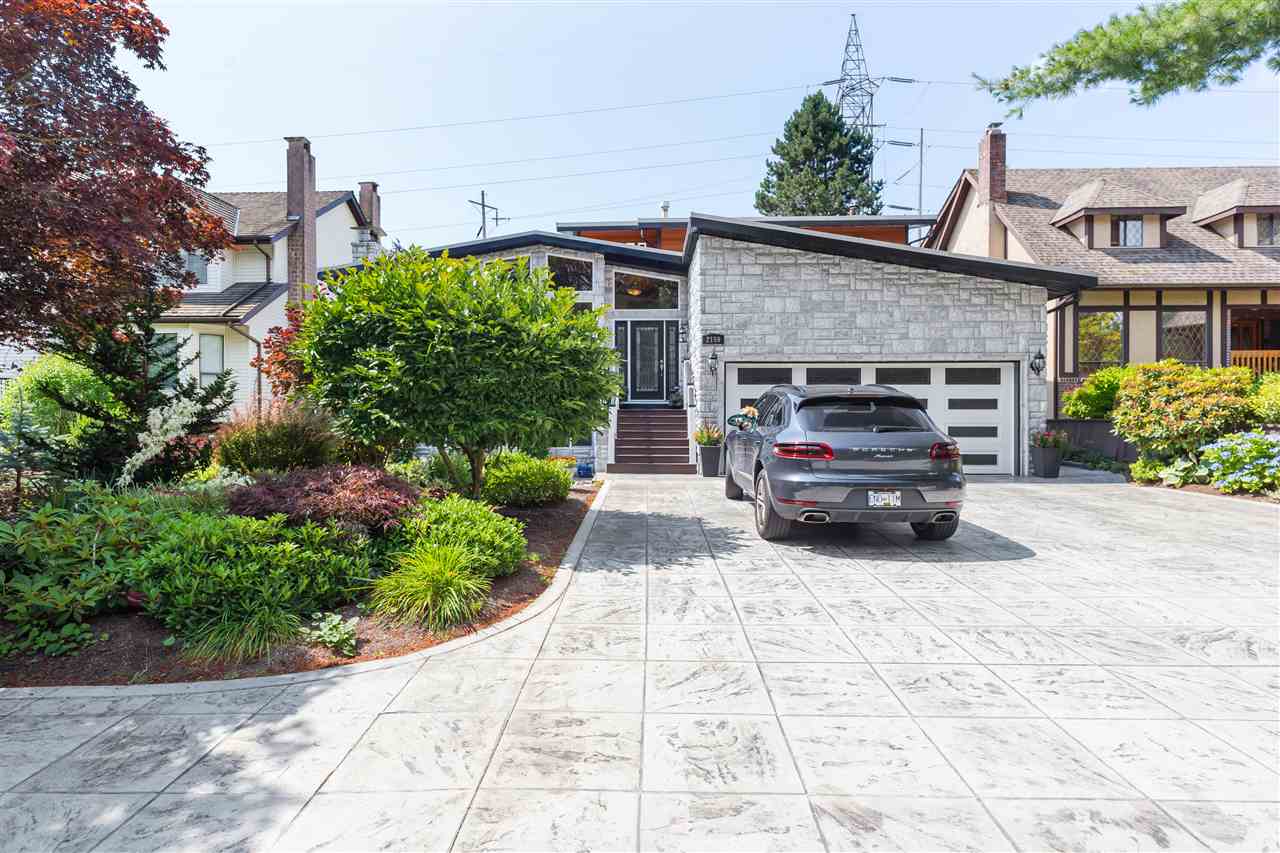 The approach, the stamped concrete driveway rising past the shrubs to the stone front and the double garage.